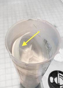 The plunger is inserted into the ink at an angle, partially descending into it. Next it will be pressed down flat (indicated by the yellow arrow).